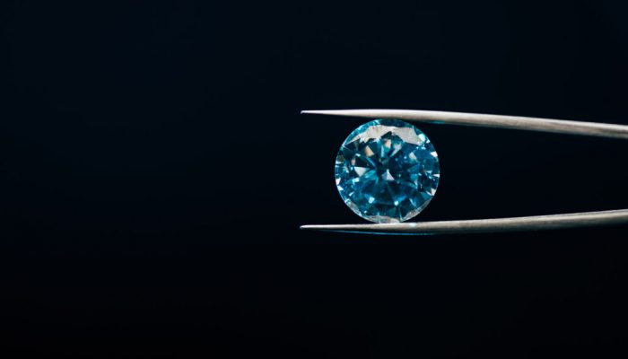 colorful blue sparkling diamond in tweezers isolated on black