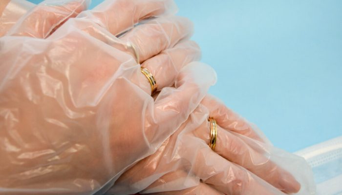 Gold wedding rings on hands in protective medical rubber disposable gloves for protection against dangerous deadly diseases of microbes and viruses by coronavirus covid-19 on a blue background.